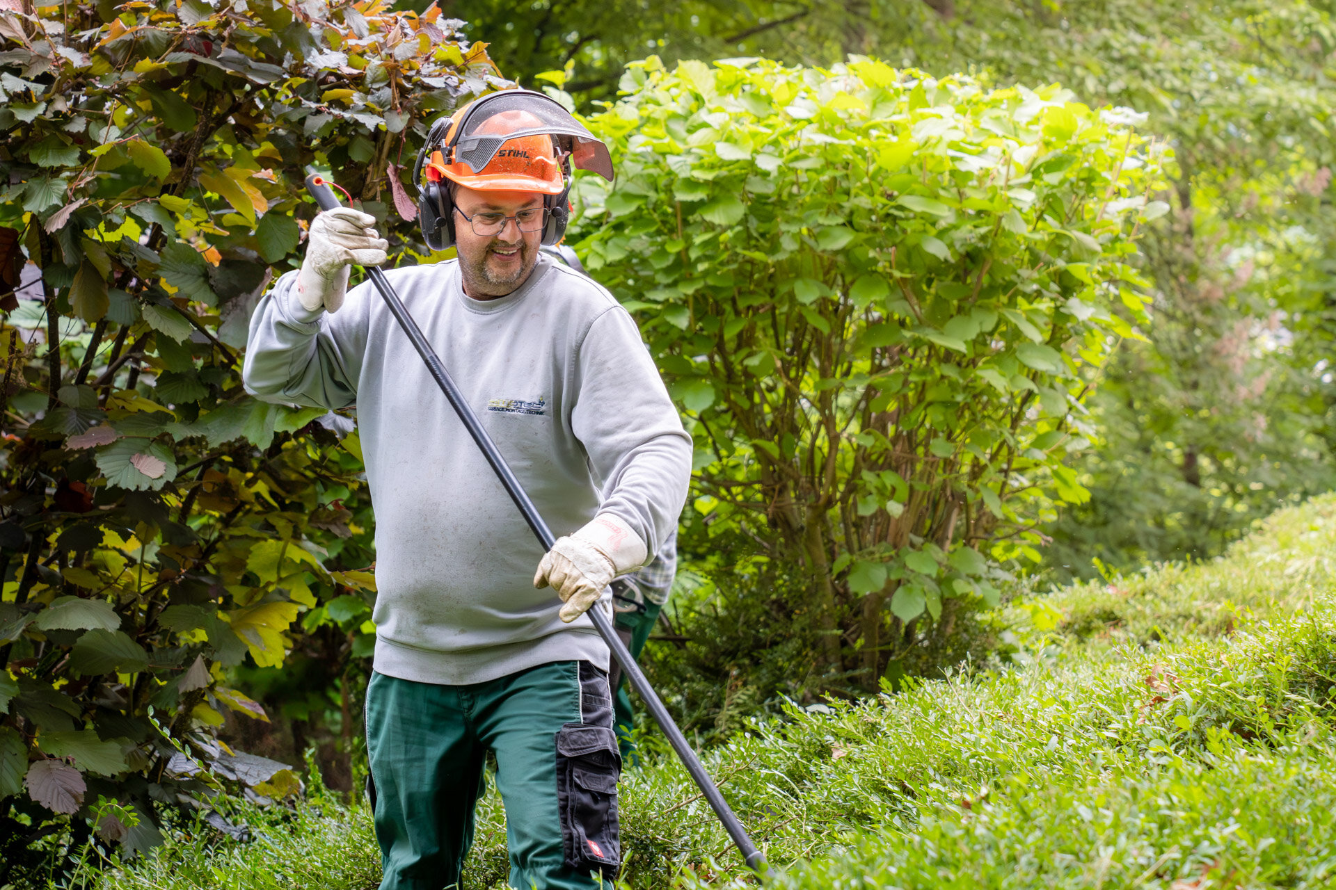 Mann steht mit einem Rechen in der in den Hecken und lächelt
